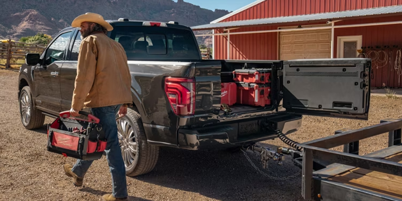 A guy walking away from his black Ford F-150 truck with a toolbox in hand on a farm.