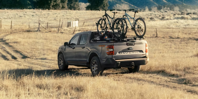 A Ford Maverick driving through a field with bikes on a rack over the truck bed